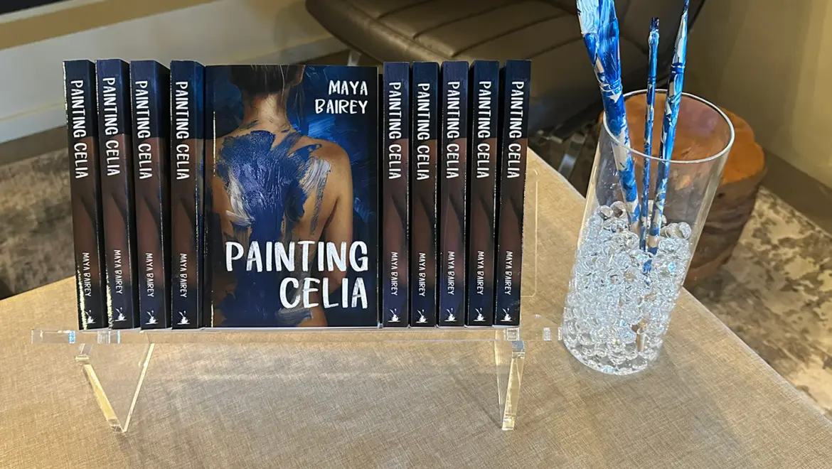 a display of paperback books sit on a table by a vase filled with paintbrushes